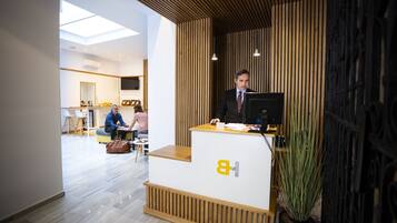 A reception desk with a logo, a man standing behind it, and a plant to the right.