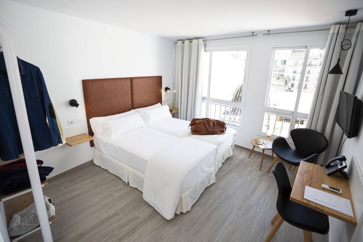 A hotel room with a large bed, a desk with a chair, a TV, and a window with curtains.