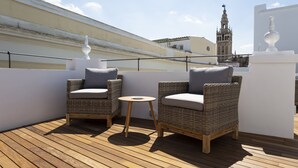 Una terraza de madera con mobiliario de mimbre y una pequeña mesa redonda.