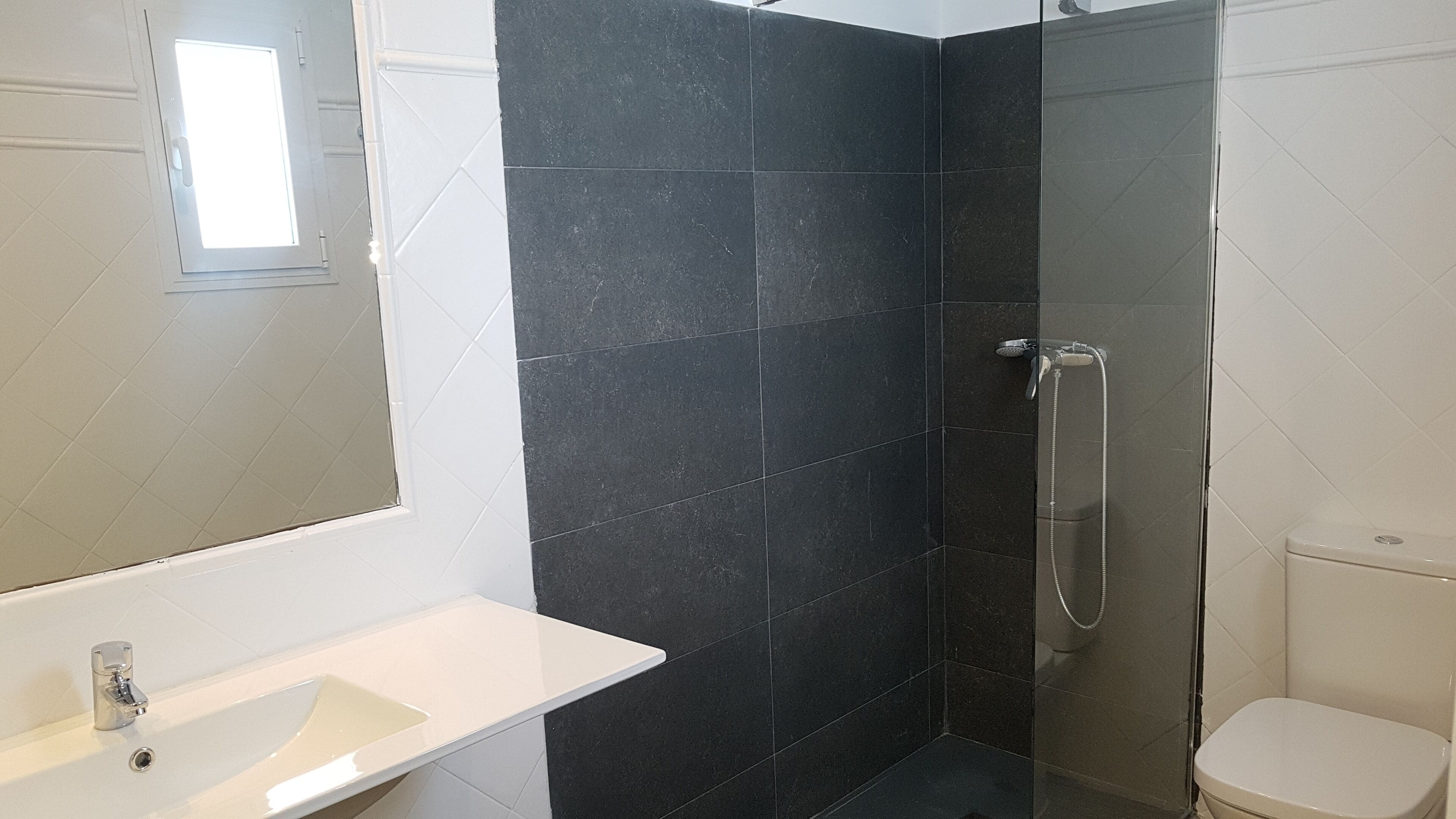 Un baño con lavamanos blanco, ducha con cabezal de ducha de mano y retrete.