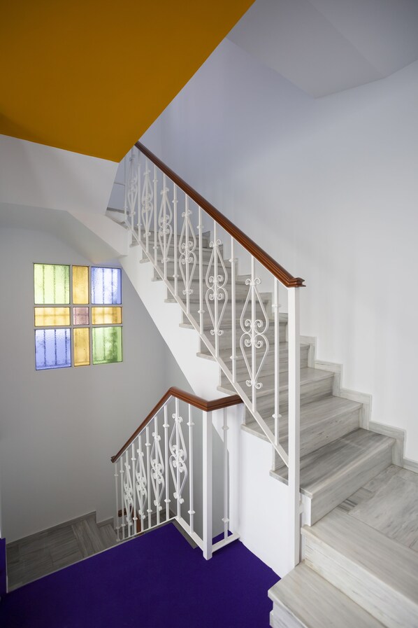 Una escalera con barandas blancas y pasamanos de madera, que conduce a un rellano con alfombra púrpura.