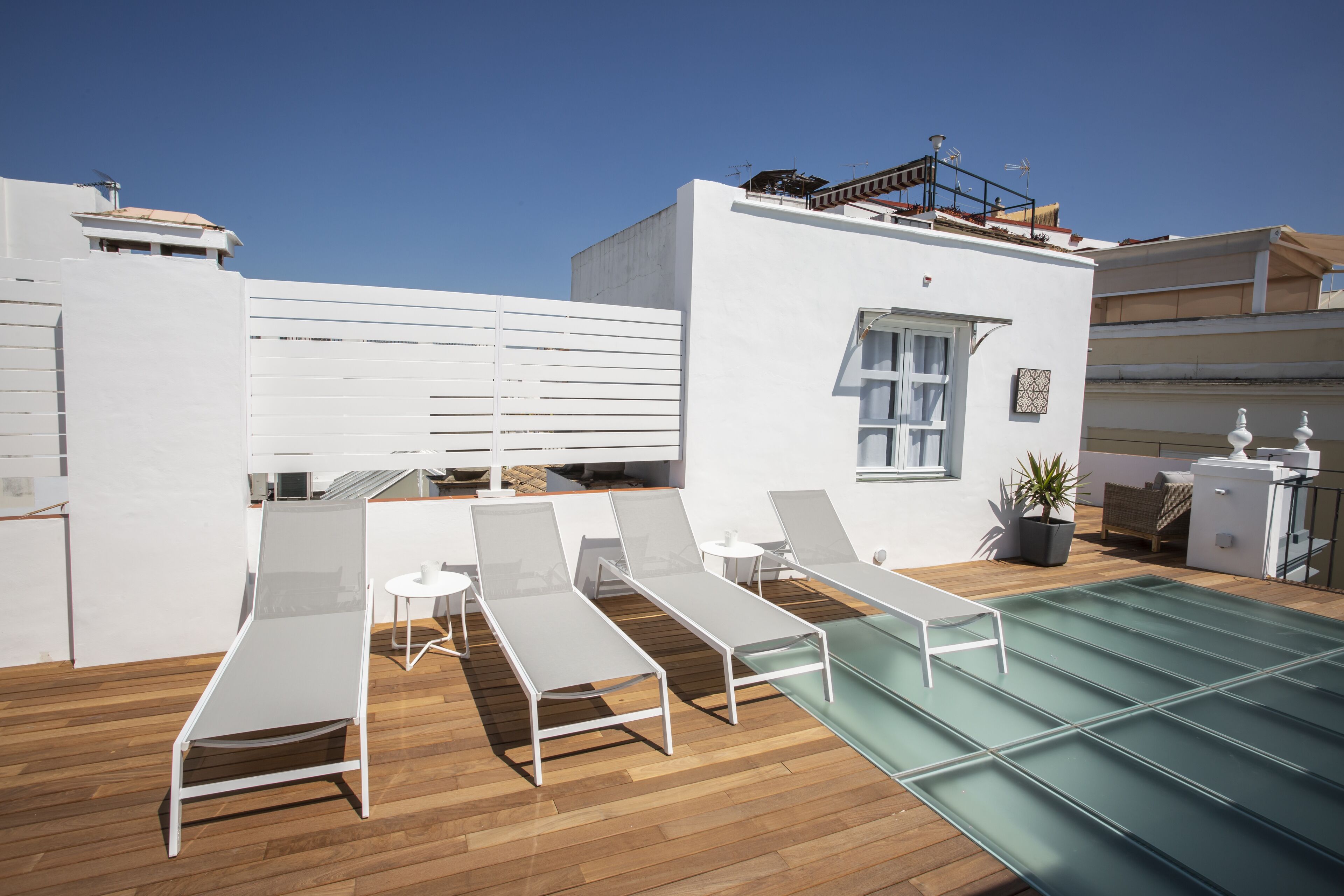 A rooftop terrace with white lounge chairs, a small table, and a pool.