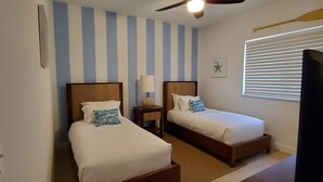 Ein Hotelzimmer mit zwei Einzelbetten, einem Deckenventilator, einem Nachttisch mit Lampe, einer Dekoration mit Seestern und einem Fenster mit Jalousien.