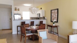 Ein Essbereich mit einem runden Tisch, Stühlen und einer Chandelüster. Im Hintergrund ist eine Küche mit Schränken und einem Kühlschrank zu sehen.
