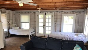A room with a wooden ceiling, two beds, a dark sofa, and a window.