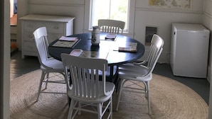 A dining area with a round table, white chairs, a chandelier, a map on the wall, and a refrigerator.