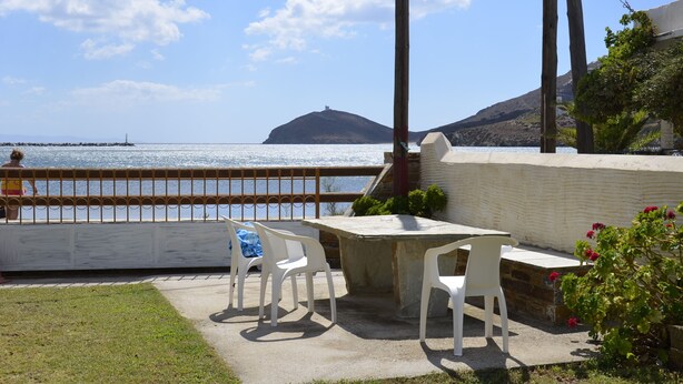 A patio with a stone table and white chairs, overlooking a body of water and a distant hill. - House Near Sea - Andros (Andros)