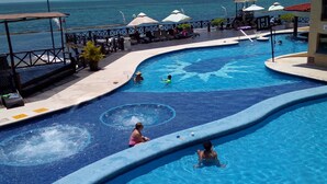 A swimming pool with a view of the sea, lounge chairs, umbrellas, and a lifeguard stand.