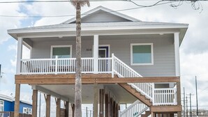 A two-story house with a balcony, a palm tree in front, and a wooden deck. - JoJo's Heaven - in town Port Aransas, private pool. 4 BR/3bath. Perfect getaway! (Port Aransas)