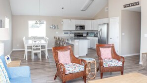 A spacious living area with a dining table, two wicker chairs, a small round table, and a kitchen in the background. - JoJo's Heaven - in town Port Aransas, private pool. 4 BR/3bath. Perfect getaway! (Port Aransas)