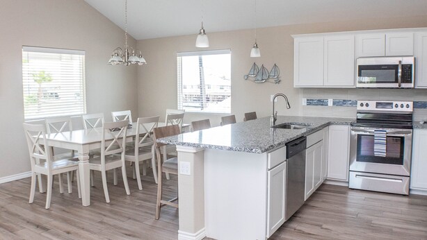 A kitchen with white cabinets, a granite countertop, a built-in oven, and a dining area with white chairs. - JoJo's Heaven - in town Port Aransas, private pool. 4 BR/3bath. Perfect getaway! (Port Aransas)
