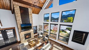 Un amplio salón con chimenea de piedra, ventanas grandes que ofrecen vistas panorámicas y una zona de estar acogedora.