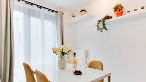Een eethoek met een tafel gedekt voor twee personen, een bloevas, een fles wijn en een schaal fruit.