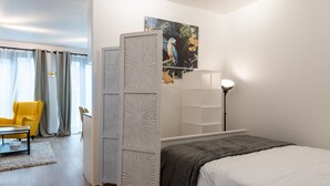 Een moderne slaapkamer met een bed, bureau, stoel en een groot raam met gordijnen.