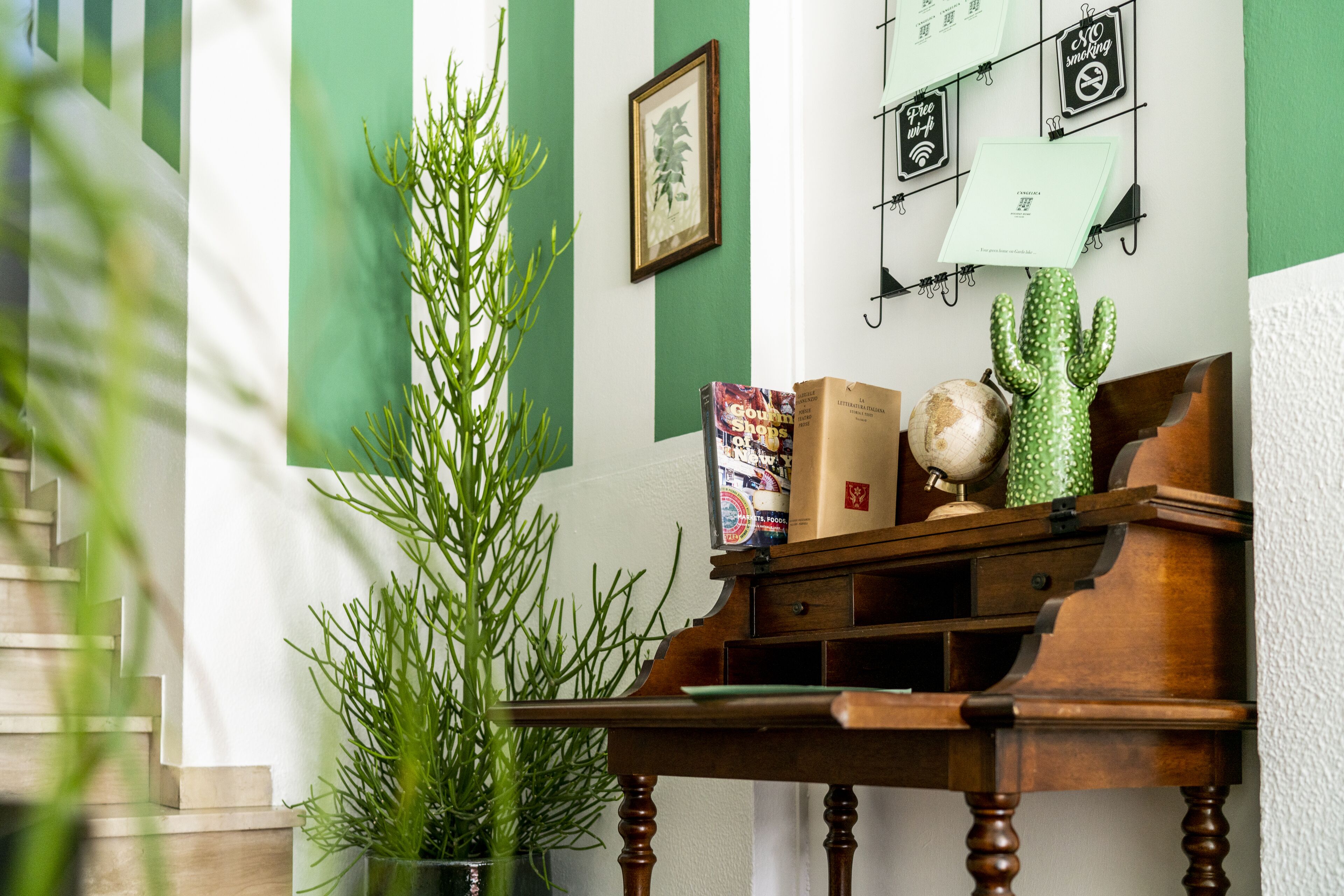 Un bureau en bois orné d’un globe terrestre et d’un cactus, d’un tableau encadré et d’une plante verte.
