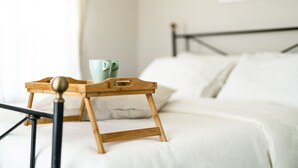 Un lit avec une literie blanche, une table de chevet en bois sur laquelle se trouve un plateau, et deux tasses vertes posées dessus.