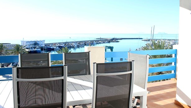 Una terraza con sillas blancas y vistas a un puerto deportivo con barcos.