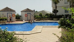 Zona de piscina con dos edificios pequeños, uno con un flotador salvavidas, y una persona caminando.