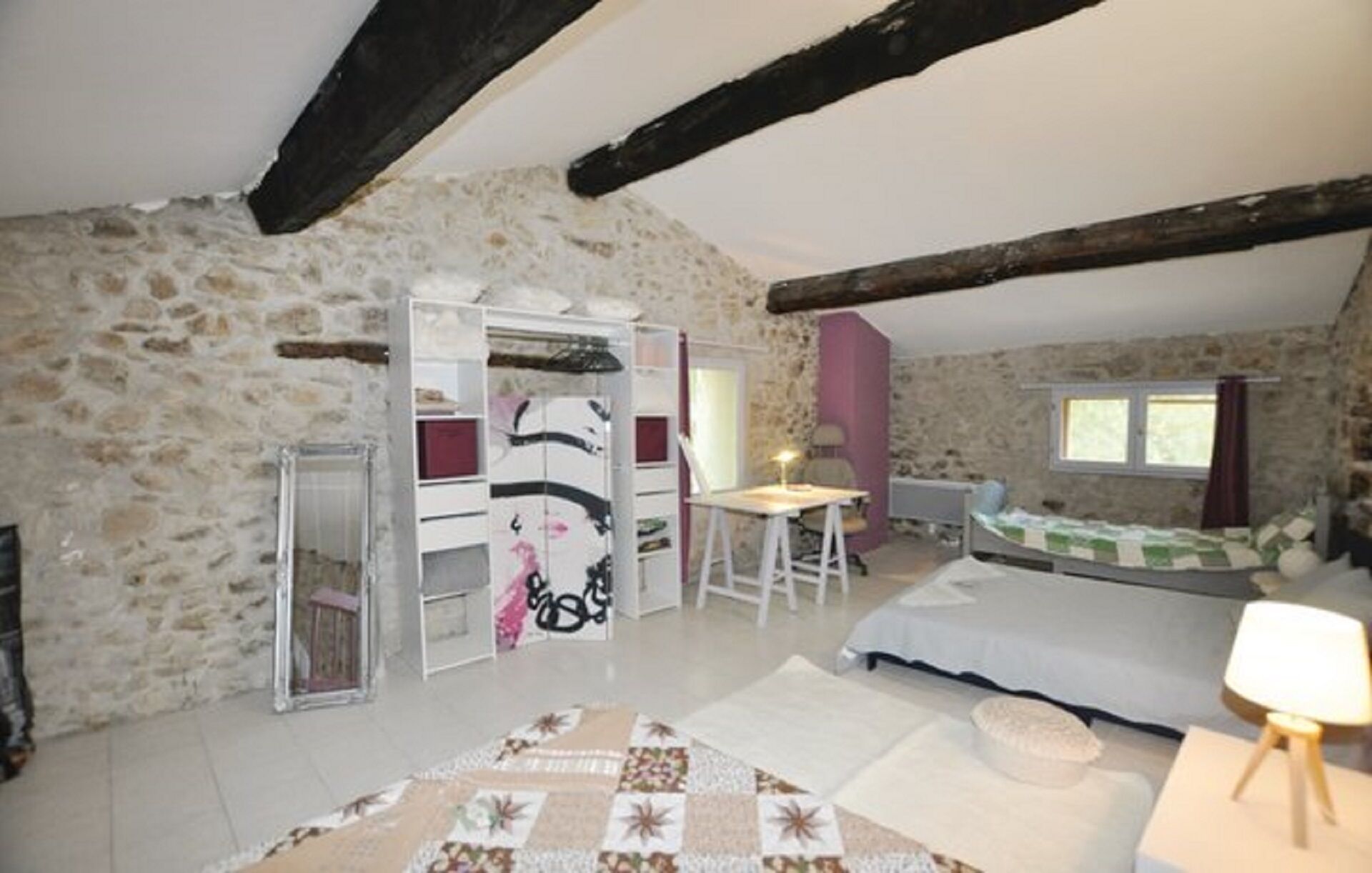 A bedroom with stone walls, a bed, a desk, and a wardrobe.