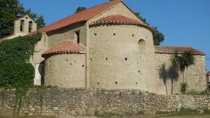 A historic building with a red-tiled roof, a stone wall, and a small bell tower.