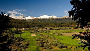 En golfbana med en bergskedja i bakgrunden, omgiven av täta skogar och bostadshus.