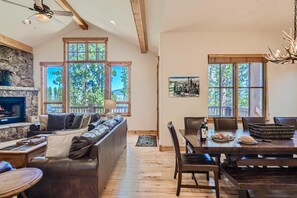 Ein geräumiges Wohnzimmer mit Kamin, einem Essbereich mit Holztisch und -stühlen sowie großen Fenstern mit Blick auf Bäume.