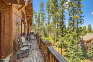 A wooden deck with chairs and a grill, surrounded by tall pine trees.