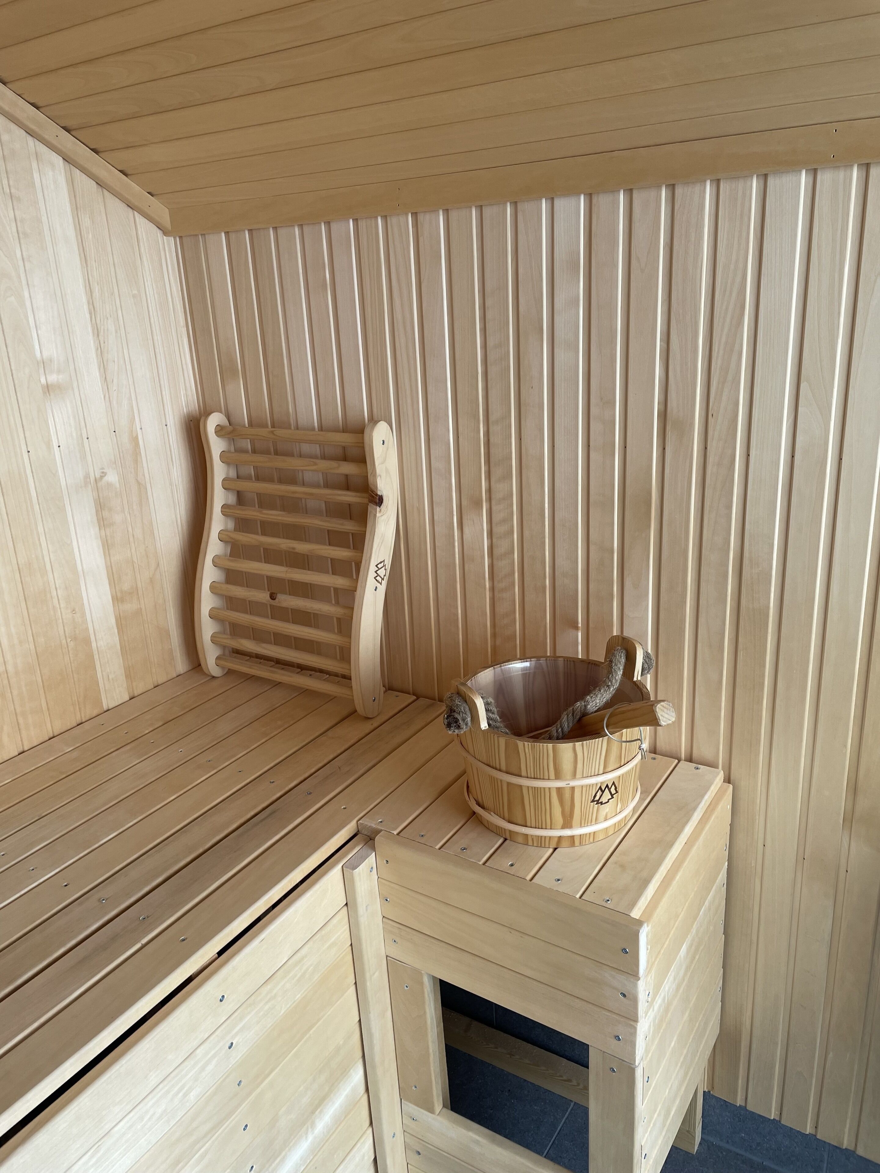 A wooden sauna with a bench, a wooden tub, and a wooden wall with slats.