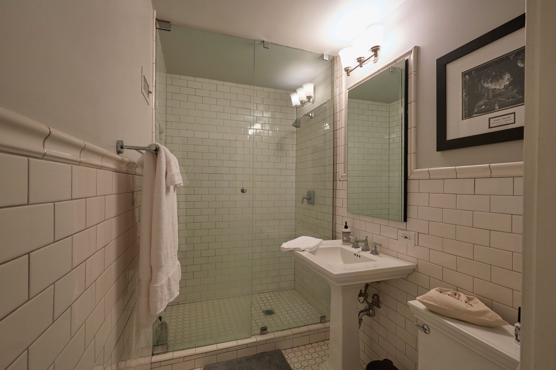 Een moderne badkamer met een glazen douchecabine, witte betegelde wanden, een wastafel en een spiegel.