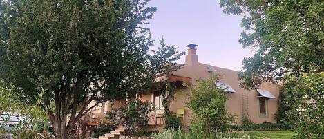 A house with a sloped roof, a chimney, and a garden with various plants and a tree.