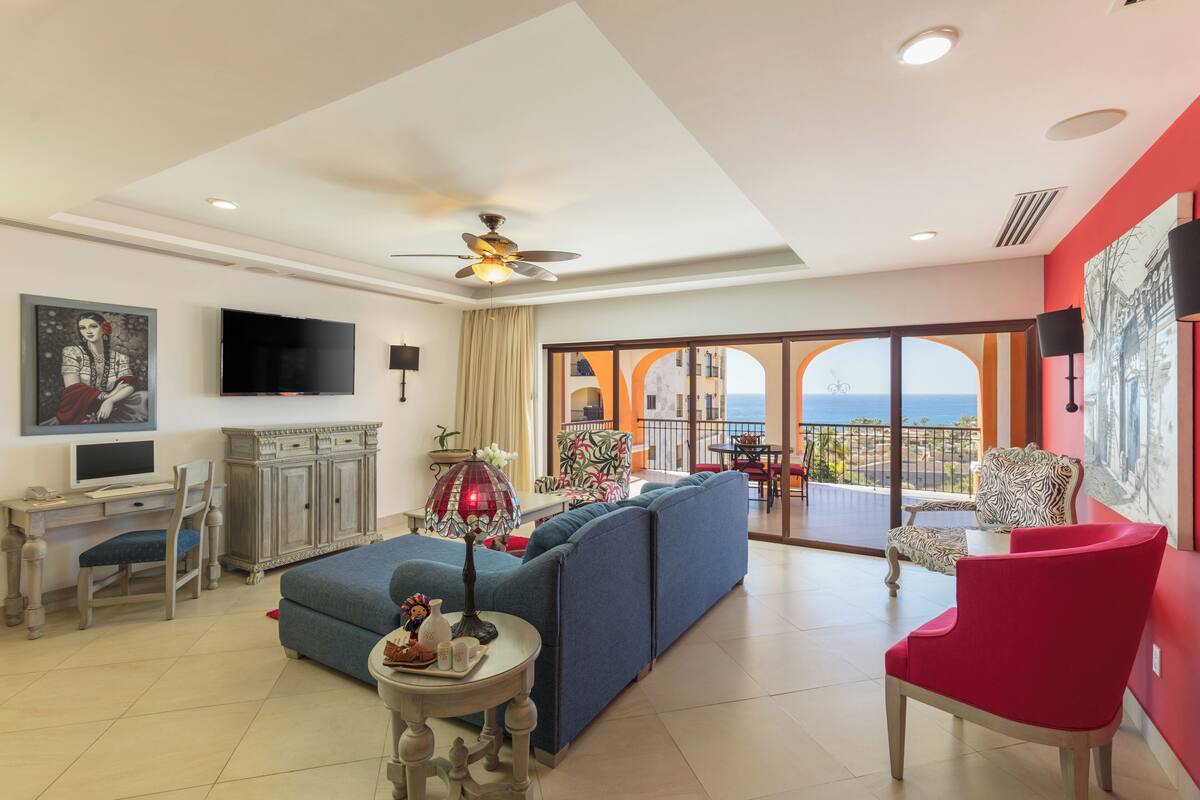 A spacious living room with a sofa, a red chair, a TV, and a balcony with a view.