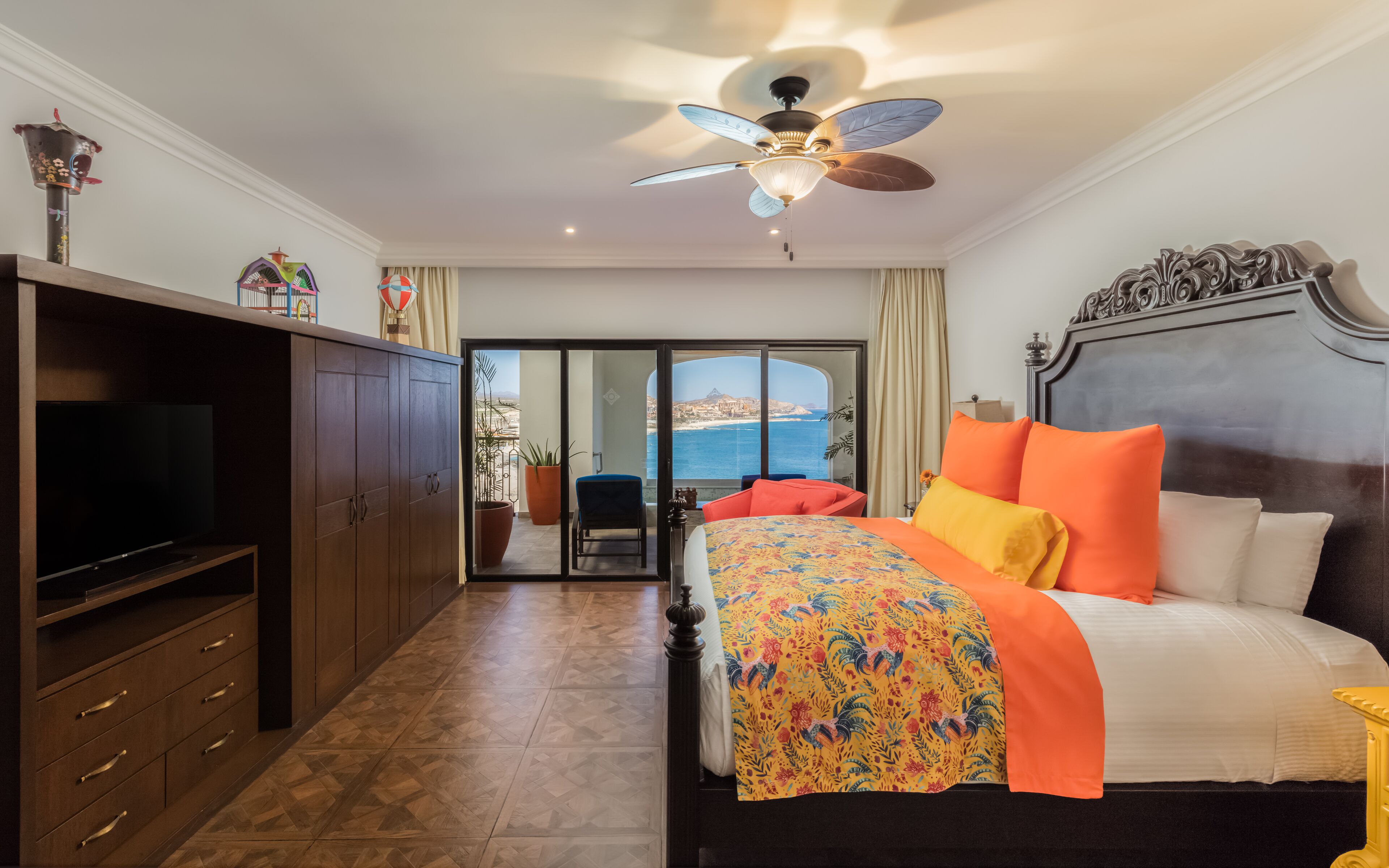 Ein Hotelzimmer mit Bett, Fernseher, Kleiderschrank und einem Balkon mit Meerblick.