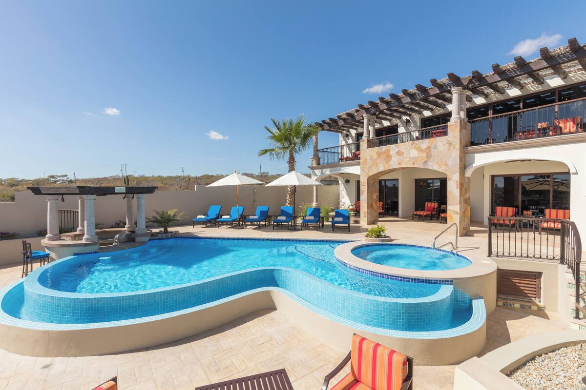 A swimming pool with blue tiles, lounge chairs, and umbrellas.