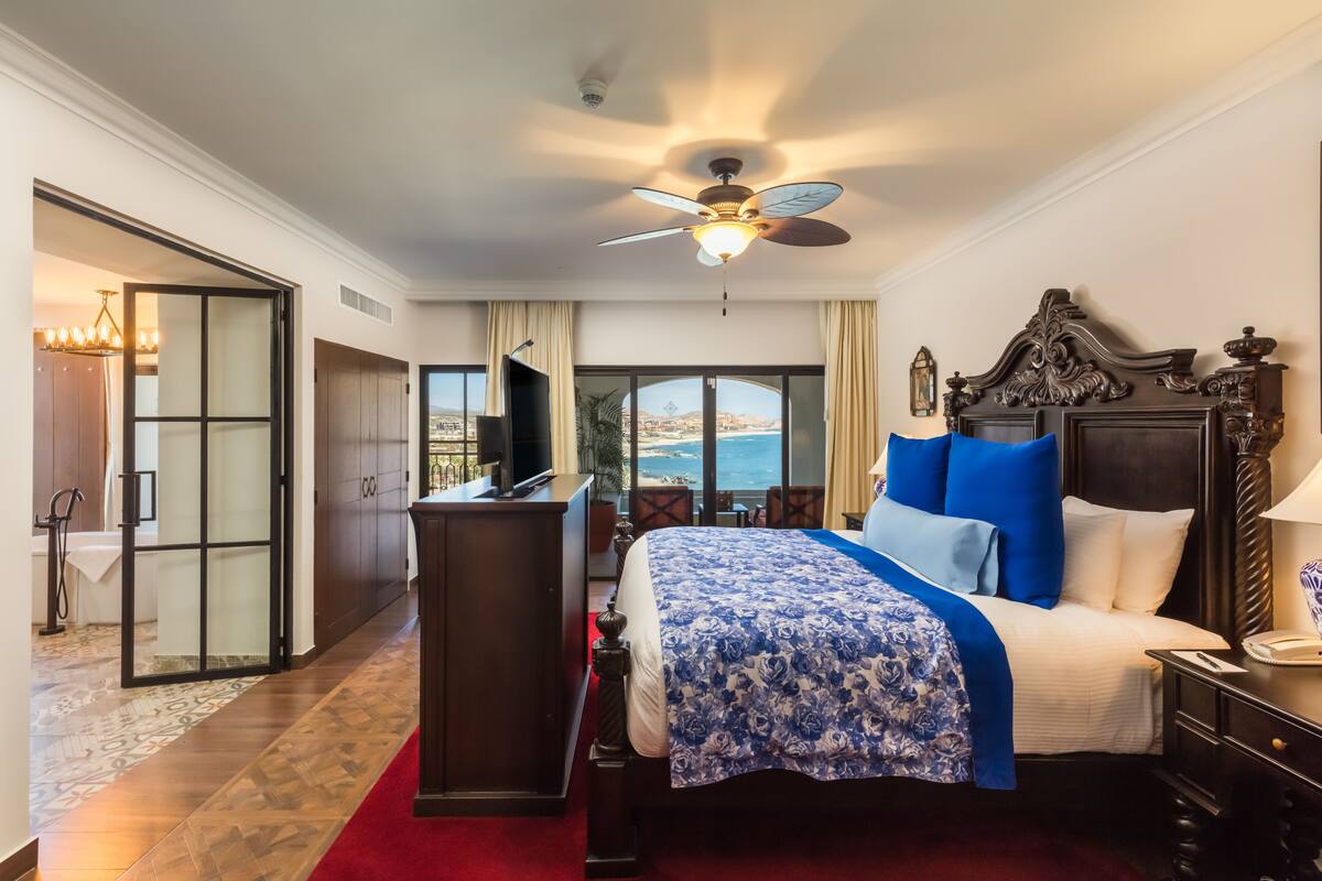 A hotel room with a large bed, a ceiling fan, a desk, and a view of the ocean.