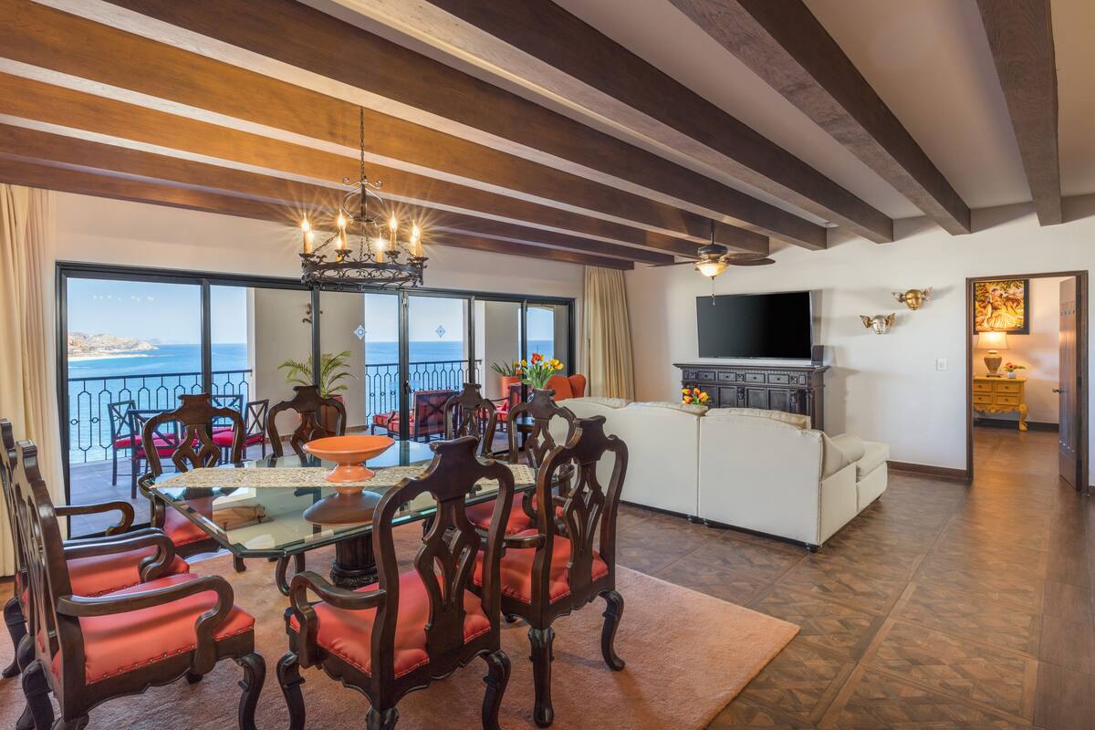 A spacious living room with a dining area, large windows overlooking the sea, a flat-screen TV, and a fireplace.