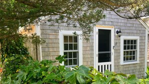 A house with a grey exterior, white trim, and two windows with white shutters.