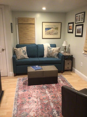 Un salon avec un canapé bleu, un tapis à motifs, une petite table d’appoint avec une lampe et un tableau encadré au mur.
