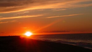 A sunset over a beach with the sun setting on the horizon.