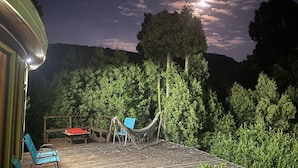 Um deck com rede, cadeiras e mesa sob um céu noturno com lua visível.
