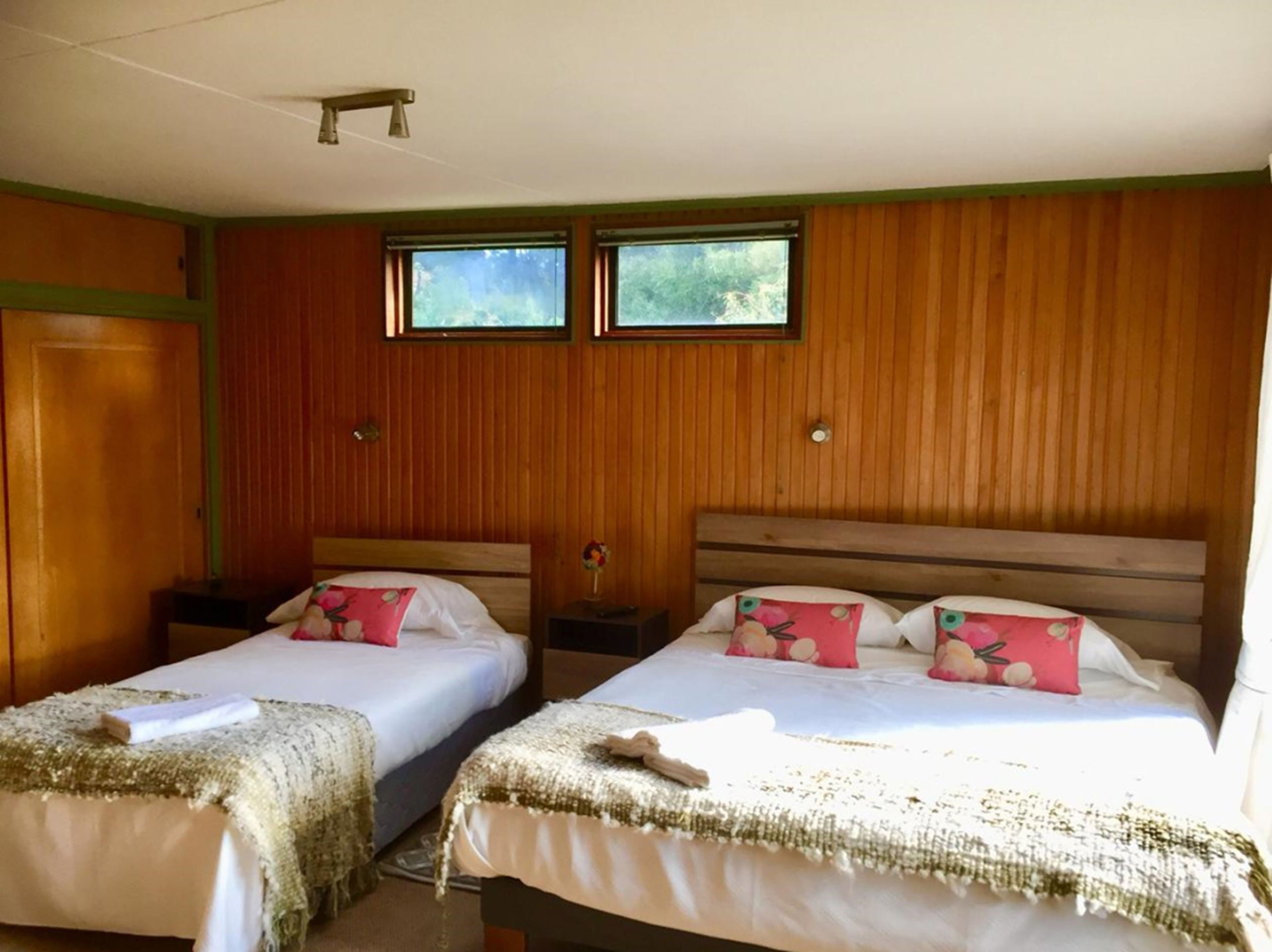 A room with two beds, wooden walls, and two windows.