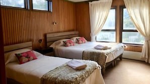 Quarto com duas camas, painéis de madeira, janela com cortinas e mesa de cabeceira com abajur.