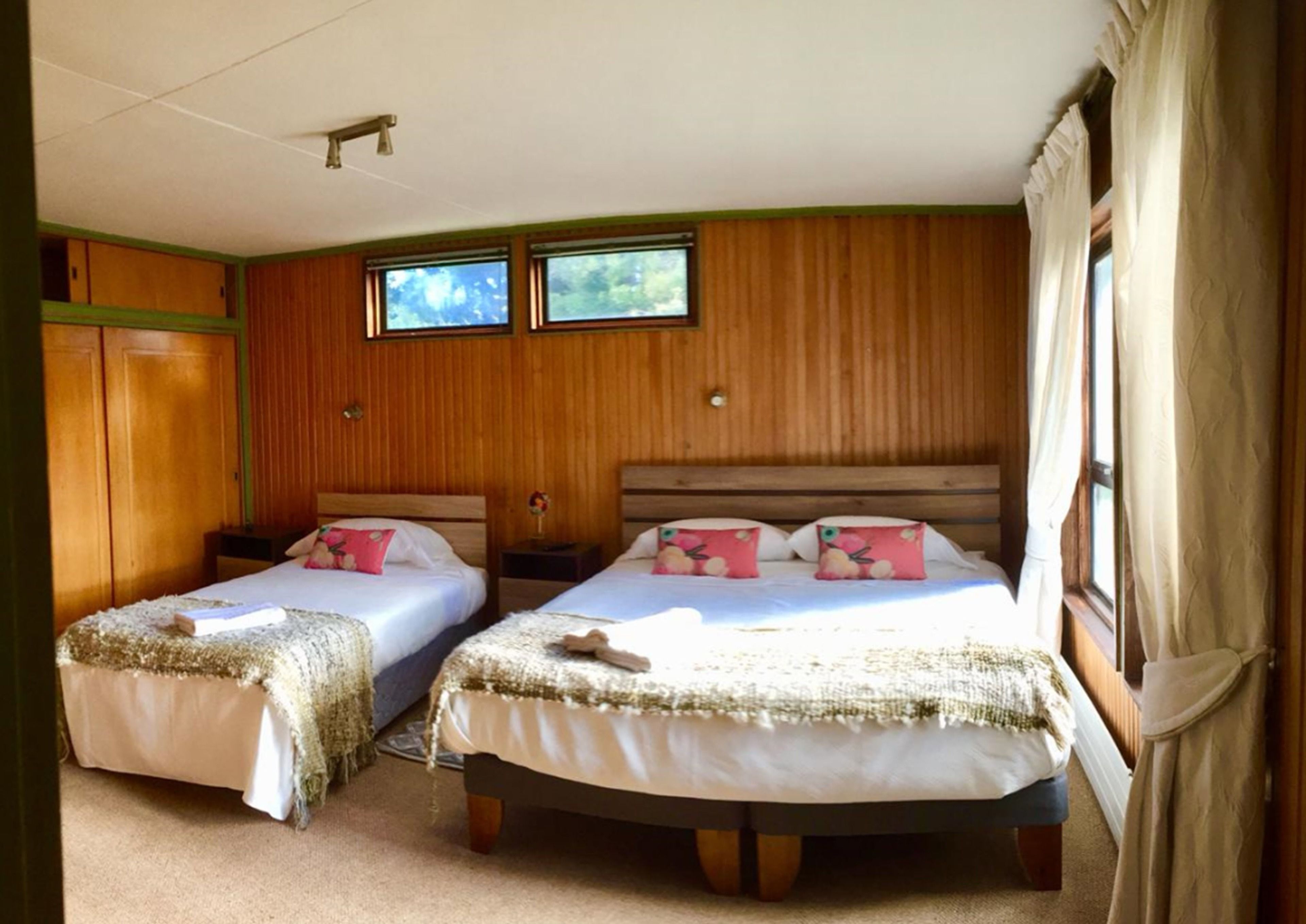 A room with two beds, wooden walls, a window, and a ceiling fan.