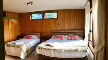 A room with two beds, wooden walls, a window, and a ceiling fan.