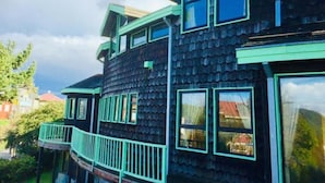 Uma casa de vários andares com fachada escura e detalhes em verde, com várias janelas e uma varanda.