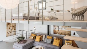 A modern loft-style living space with a mezzanine level, a grey sofa with patterned cushions, and a variety of decorative items.