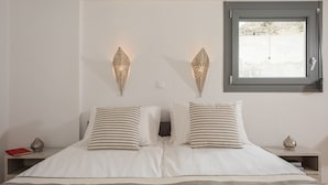 A bedroom with a bed, two bedside tables, a window, and decorative wall sconces.