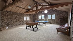 Een rustieke kamer met een tafelvoetbaltafel, een pingpongtafel, stenen muren en een schuine balkenlaag.