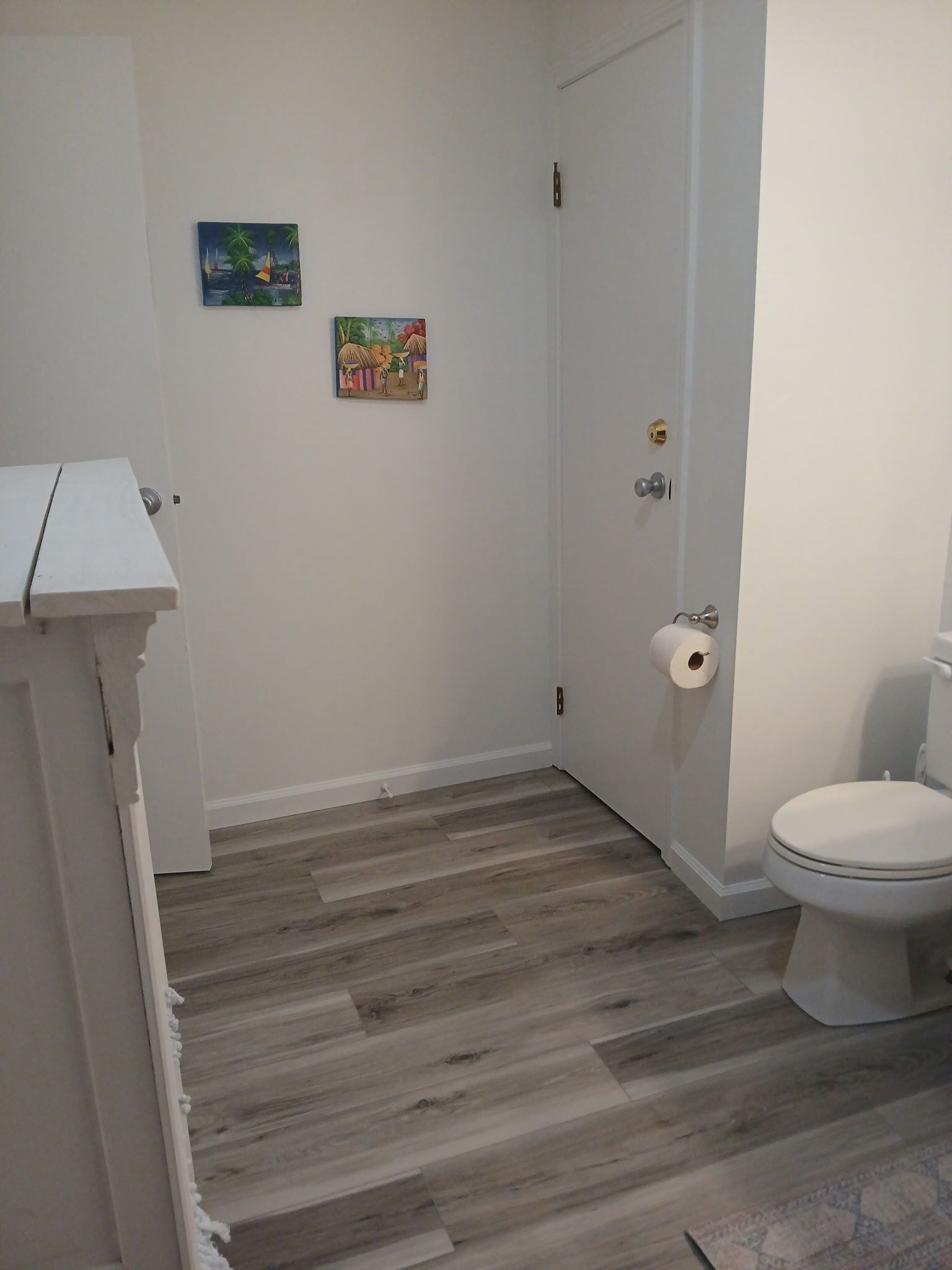 Une salle de bain avec des toilettes, un rouleau de papier toilette et un plancher en bois.