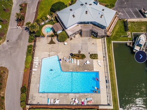 An aerial view of a property with a swimming pool, lounge chairs, and a boat dock.