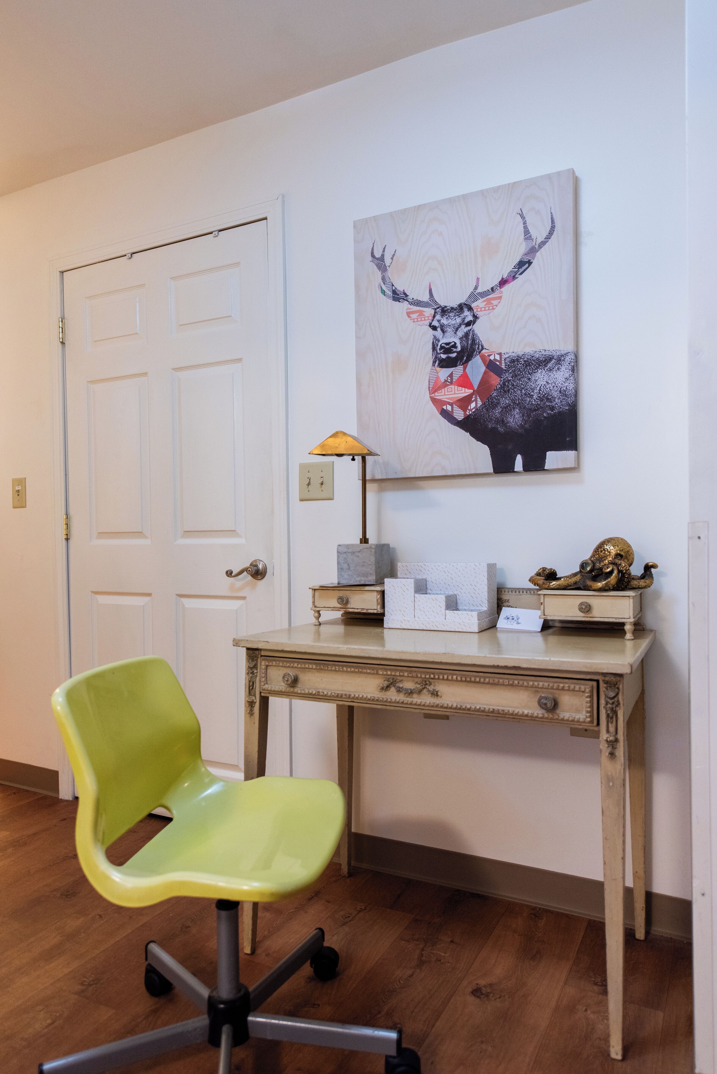 Una habitación con escritorio, una silla y una obra de arte en la pared de un ciervo.